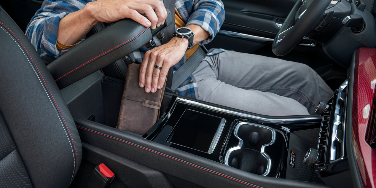 A person storing a notebook on the front row compartment of the 2025 Chevrolet Traverse SUV.