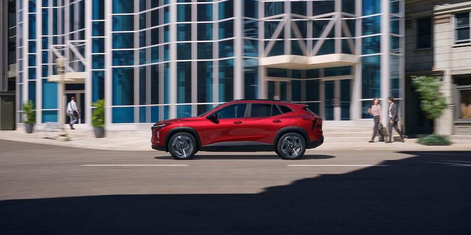 Left side profile view of the 2025 Chevrolet Trax 2RS by an office building.