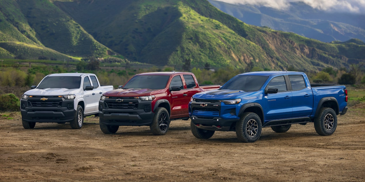 Three Chevrolet Colorado trucks parked side by side next to a mountain.