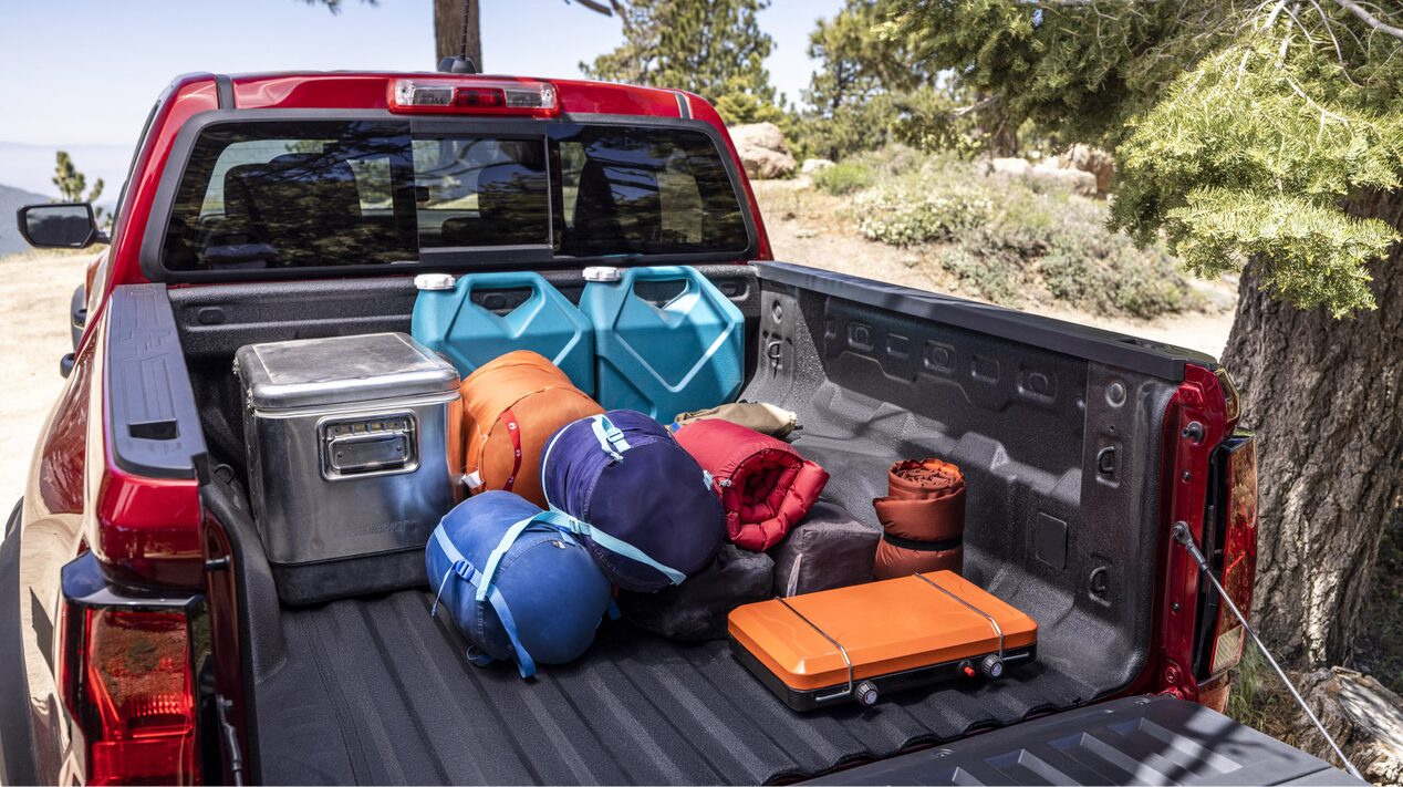 Rear view of the trunk of a 2025 Chevrolet Colorado with camping gears and other traveling equipment being stowed.