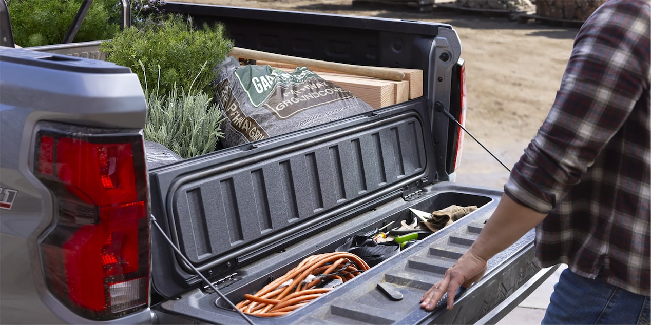 Les compartiments de rangement dans la caisse du Chevrolet Colorado 2025 commercial remplis d’outils d’aménagement paysager.