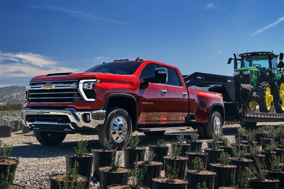 Vue latérale avant du camion de travail Chevrolet Silverado HD 2025 stationné à l’extérieur devant des plantes.