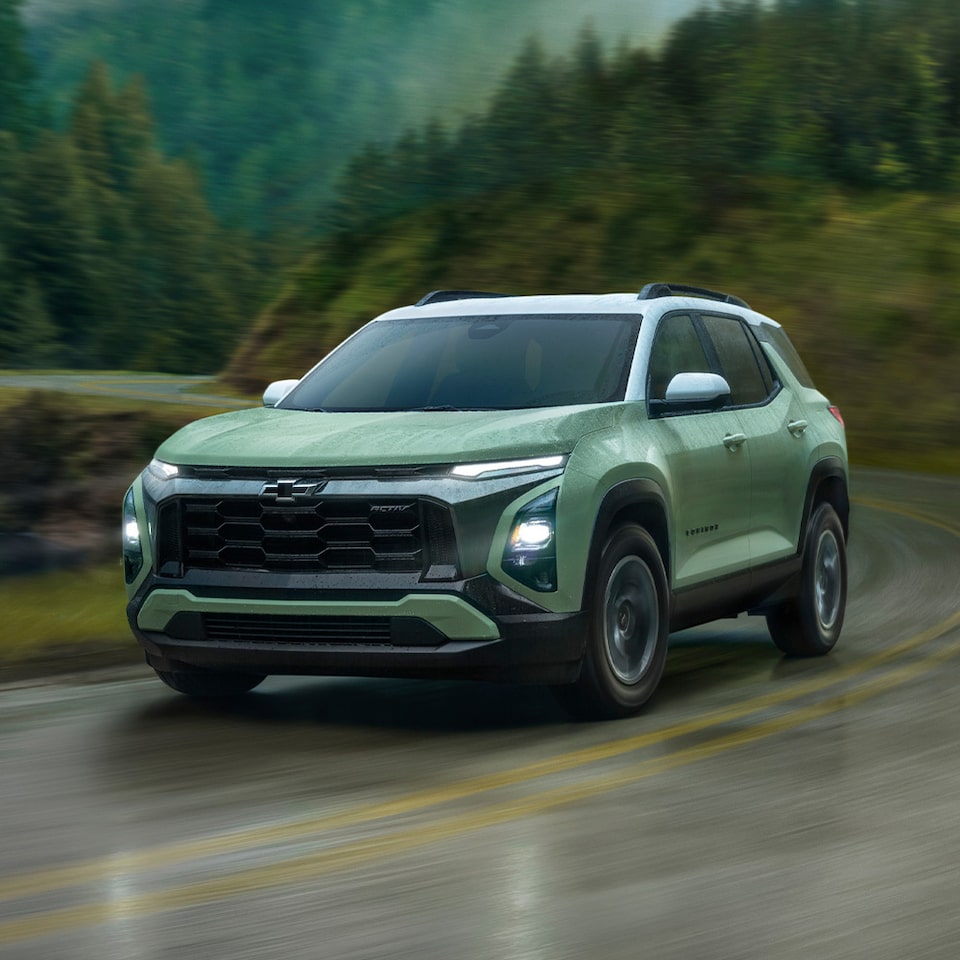 Front view of a 2025 Equinox compact SUV driving down a scenic road.