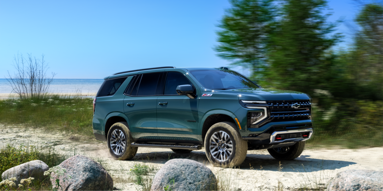 Side view of the 2025 Chevrolet Tahoe SUV driving alone near a beach.