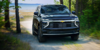 Front Three-Quarters View of the 2025 Chevrolet Tahoe SUV Driving On a Gravel Path Surrounded by Trees