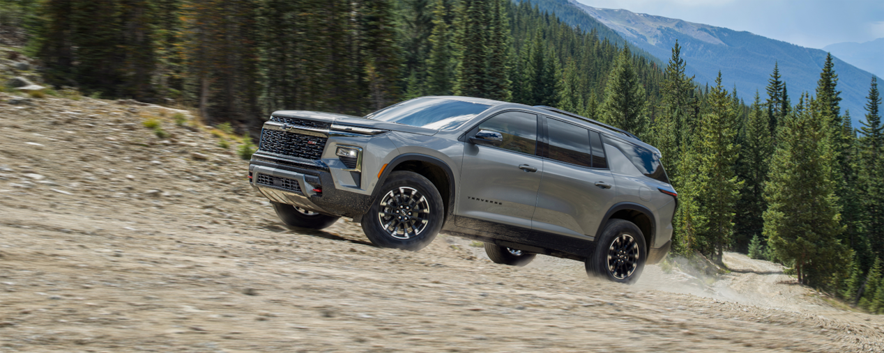 2025 Chevrolet Traverse SUV driving through a tree-lined dirt path.