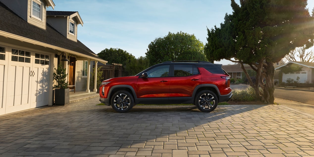 Vue latérale du Chevrolet Equinox 2026 en teinte rouge éclatant stationné devant une maison.
