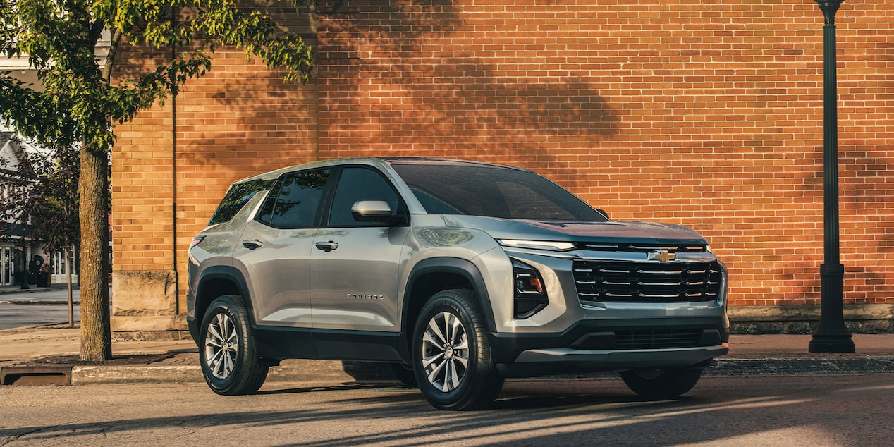 Vue latérale avant du Chevrolet Equinox LT 2026 qui passe devant un mur de briques rouges.
