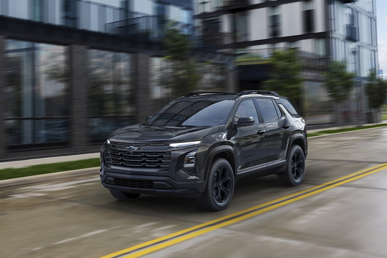 Front-side view of the 2026 Chevrolet Equinox driving past a glass building.