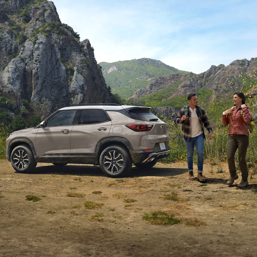 Two people walking past a 2026 Trailblazer parked in a hilly area.