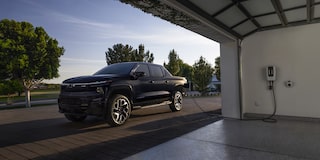 Un Chevrolet Silverado EV 2025 en train d’être rechargé à côté d’un garage pendant la journée.