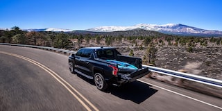 Vue latérale arrière du Chevrolet Silverado EV 2025 en mouvement sur une route de montagne.