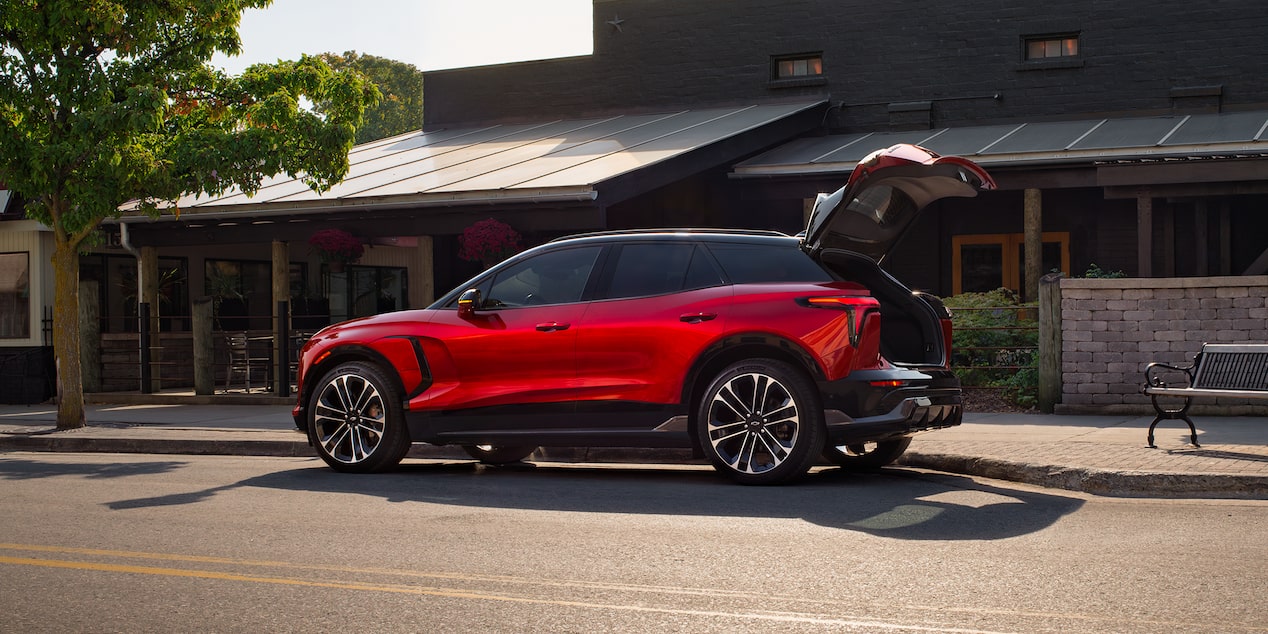 Side view of the 2026 Chevrolet Blazer EV Parked Outside a Shop with the Trunk Open.