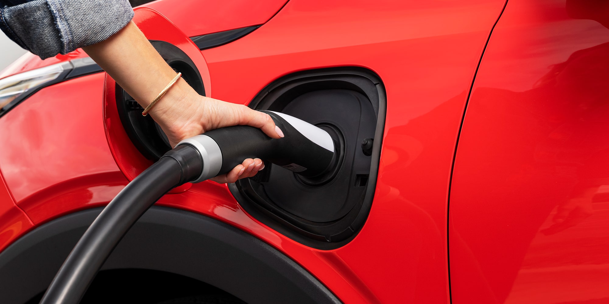 Gros plan d’une main branchant un câble de recharge dans la prise de chargement d’une Chevrolet Bolt 2027 rouge.