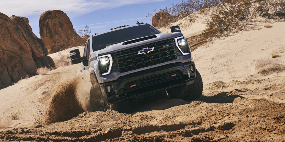 Front view of the 2025 Chevrolet Silverado HD pickup truck driving through a tough terrain.