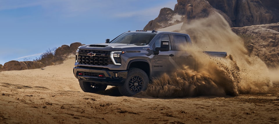 Vue latérale avant du pick-up Chevrolet Silverado HD 2025 en train de déraper sur un terrain sablonneux.