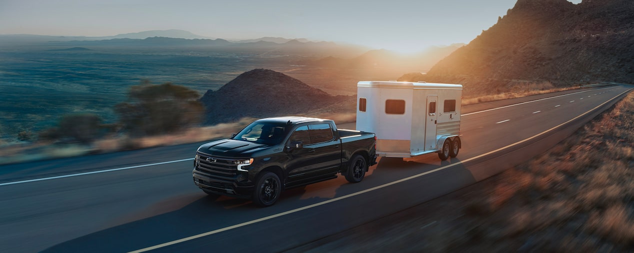 A Chevrolet pickup truck driving on the road while towing a small trailer.