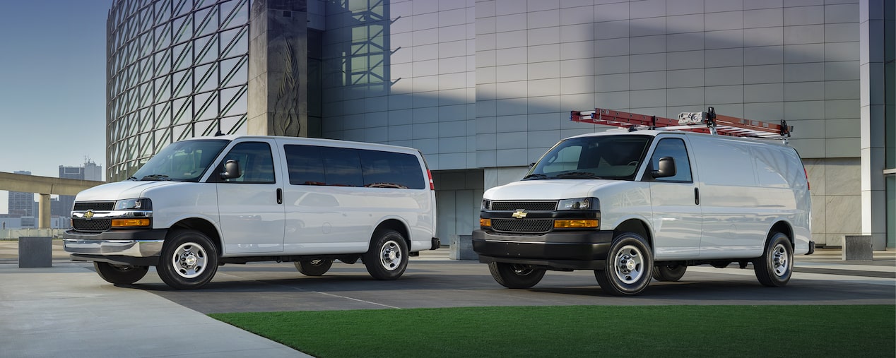 Deux fourgonnettes commerciales Chevrolet Express 2025 stationnées devant un immeuble de bureaux.
