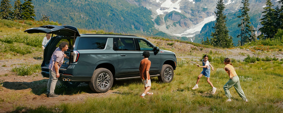 A Family Unloads Their 2025 Chevrolet Suburban While Parked in a Field Near Mountains.