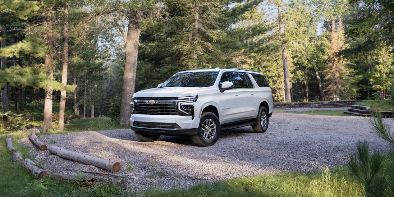 Front-side view of the 2025 Chevrolet Suburban SUV parked near a cabin.