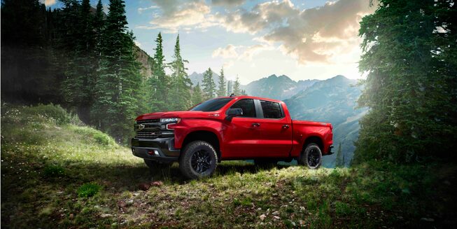 Chevrolet Silverado 1500 Crew Cab LT Trail Boss in Red Hot, 3/4 drivers side front, trees, hill, mountains.